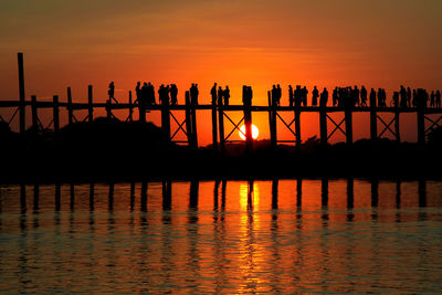 Silhouette people by sea against orange sky