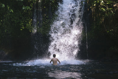 Full length of shirtless man splashing water in waterfall