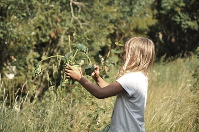 Side view of woman holding plant on field