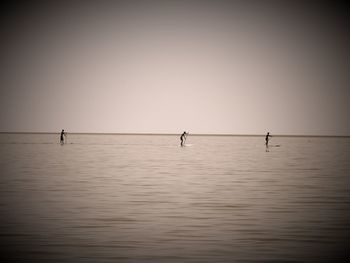 People paddleboarding in sea against clear sky