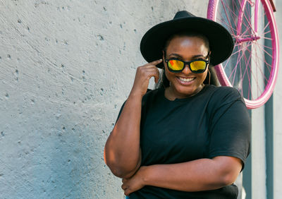 Portrait of young man wearing sunglasses while standing against wall