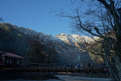People standing on footbridge over river against mountain