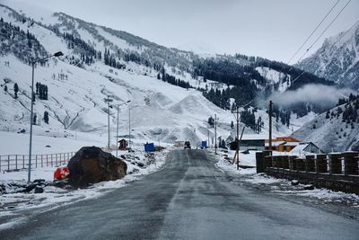 Snow covered road by snowcapped mountains against sky