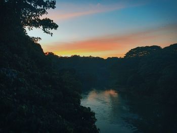 Silhouette trees by lake against sky during sunset