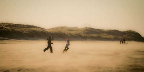 Boys running at beach against clear sky