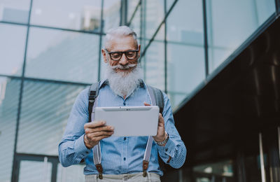 Man holding mobile phone while standing against wall