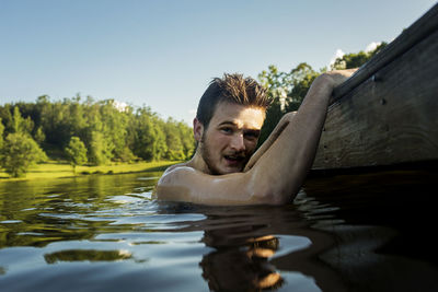 Portrait of shirtless man swimming in lake against trees and clear sky