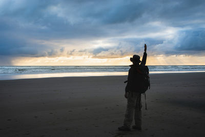 Rear view of silhouette person standing on beach against sky during sunset