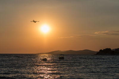 Scenic view of sea and airplane against sky during sunset