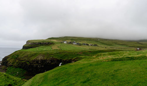 Scenic view of green landscape and sea against sky