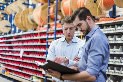 Two men with folder talking in factory storeroom