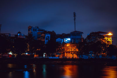 Illuminated buildings by river against sky at night