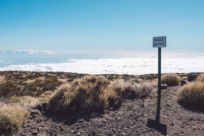 Road sign on field against sky