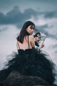 Young woman sitting on mobile phone against sky