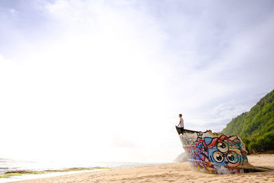 Man standing at shipwreck on beach against sky