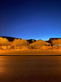 Road amidst field against clear blue sky