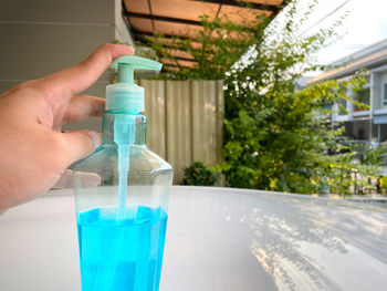 Close-up of hand holding glass bottle against water