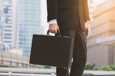 Midsection of businessman holding briefcase while standing against buildings