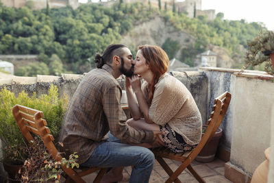 Couple kissing while sitting on chair at rooftop