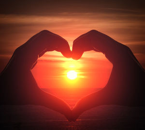 Cropped hands making heart shape against sky during sunset