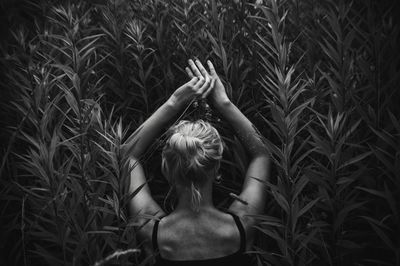 Rear view of woman with arms raised amidst plants