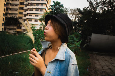 Close-up of young woman blowing stalk while standing in city