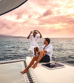 Couple sitting on yacht at sea against sky during sunset