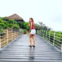 Full length of woman standing on footbridge against clear sky