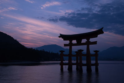 Shrine at lake against sky during sunset