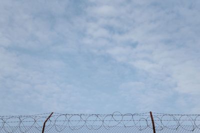 Low angle view of barbed wire fence against sky
