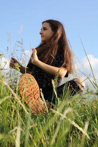 Young woman looking away while sitting on field