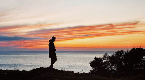Silhouette man standing on beach against sky during sunset