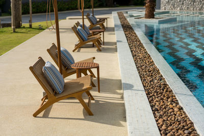 Wooden pool chair in the edge of the swimming pool with shade of light at summer time