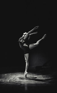 Full length of woman dancing against black background