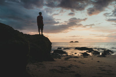 Rear view of man standing on rock against sky during sunset