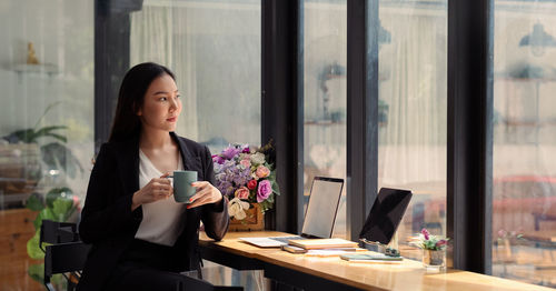 Portrait of young woman using mobile phone while standing in office