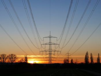 Low angle view of silhouette electricity pylon on field against sky during sunset