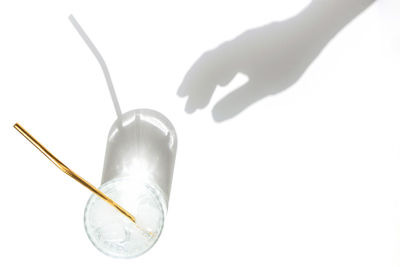 Transparent glass of water with reusable metal eco straw in sunlight with shadows and female hand.