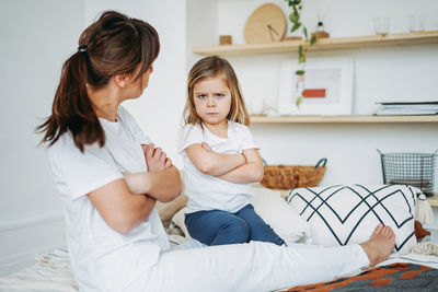 Woman looking at daughter sitting with arms crossed
