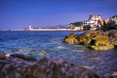 Sea by buildings against blue sky