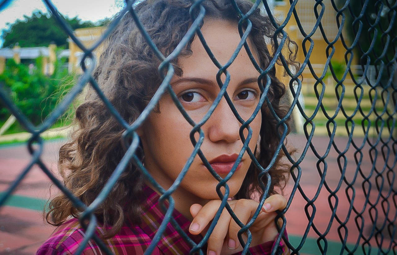CLOSE-UP PORTRAIT OF A GIRL THROUGH CHAINLINK FENCE