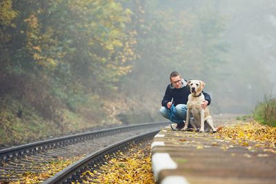 Young man with dog crouching by railroad track