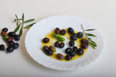 A white plate with oil and several ripe olives in it.