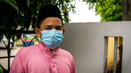 Portrait of young man standing against pink wall