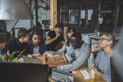 Smiling colleagues eating pizza while working at workplace