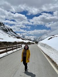 Woman standing on road by snowcapped mountain against sky