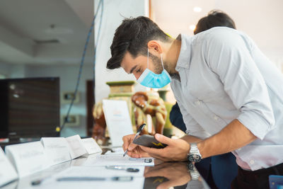 Young man wearing mask writing in office