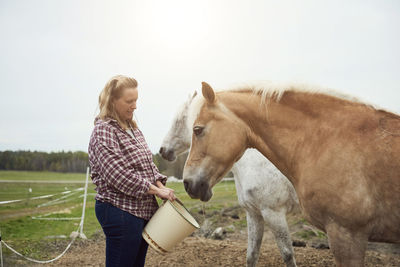 Female farmer feeding horse on field