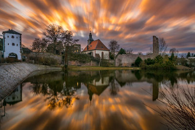 Church against cloudy sky reflecting on lake during sunset