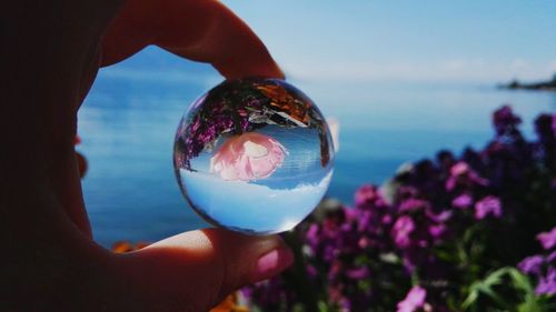 Close-up of hand holding crystal ball against sea